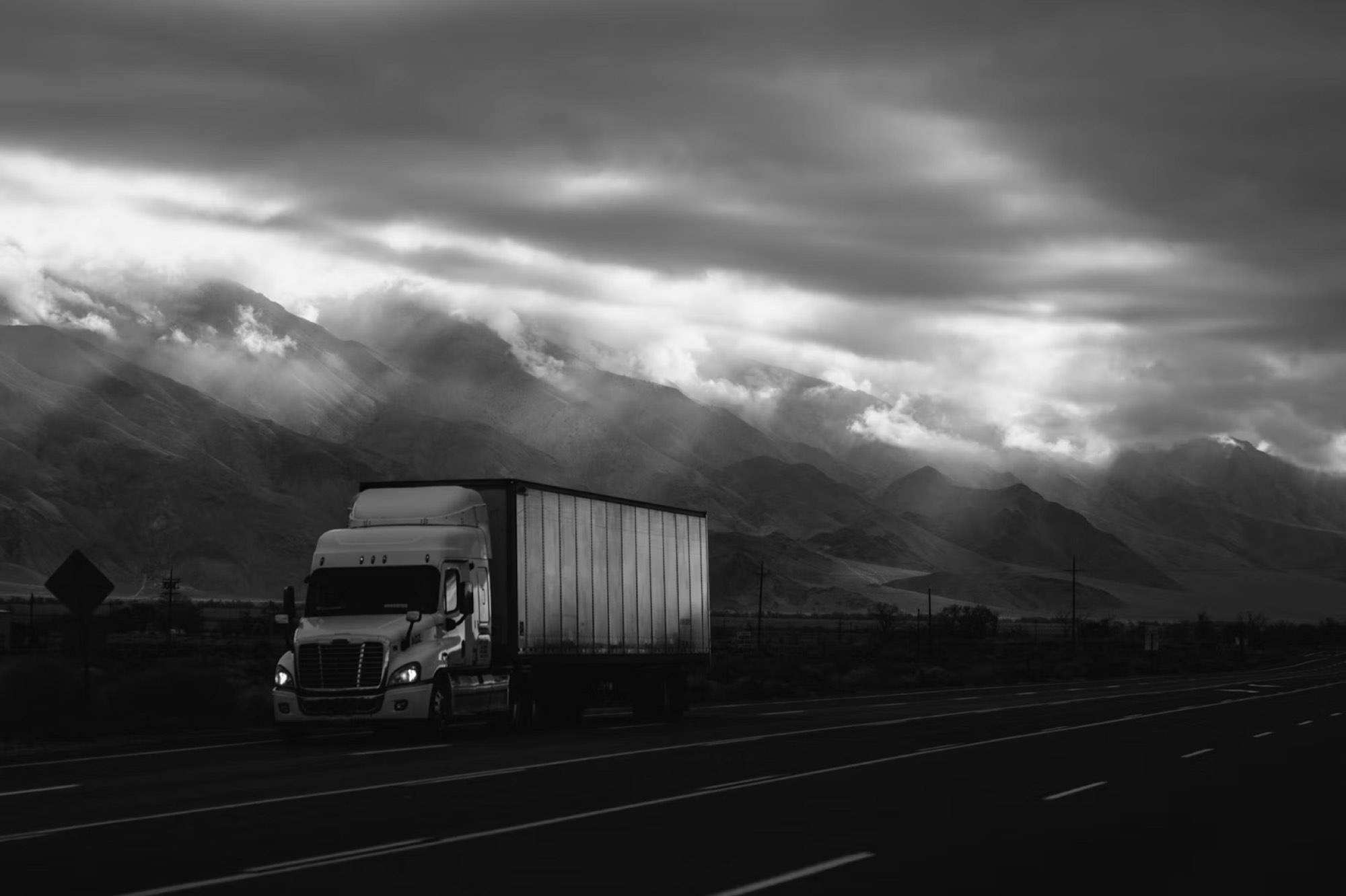 A freight truck on a mountain highway under heavy clouds